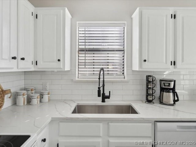 kitchen with tasteful backsplash, light stone countertops, white dishwasher, white cabinetry, and a sink