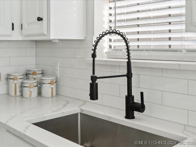 details featuring tasteful backsplash, a sink, light stone counters, and white cabinets