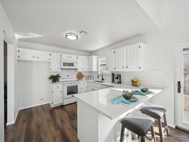 kitchen featuring a peninsula, white appliances, white cabinets, and a sink