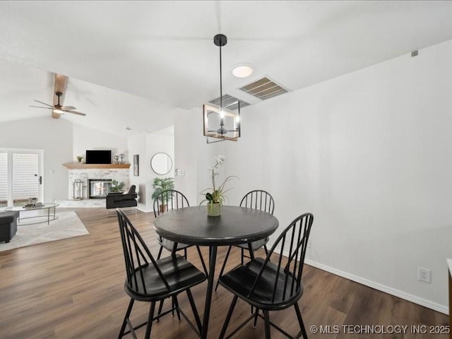 dining space featuring visible vents, a glass covered fireplace, vaulted ceiling, wood finished floors, and baseboards