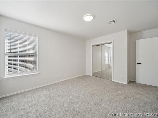 unfurnished bedroom with light carpet, baseboards, visible vents, and a closet