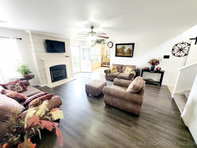 living room featuring dark wood-style flooring, visible vents, a fireplace with raised hearth, stairway, and ceiling fan