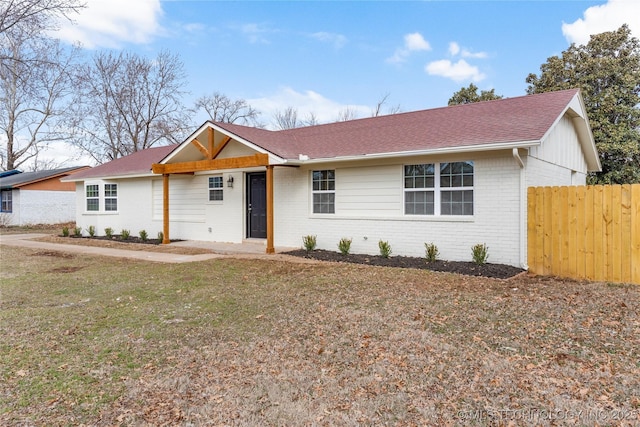 ranch-style house with roof with shingles, a front yard, fence, and brick siding