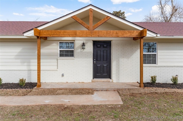 entrance to property with a shingled roof and brick siding