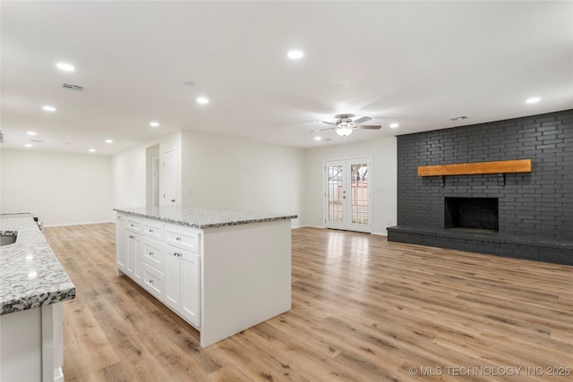 kitchen featuring light stone counters, white cabinets, open floor plan, a brick fireplace, and a center island