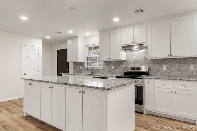 kitchen with under cabinet range hood, a kitchen island, visible vents, white cabinetry, and electric stove