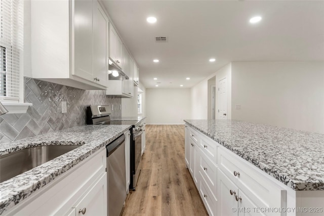 kitchen with light stone counters, stainless steel appliances, visible vents, white cabinetry, and light wood finished floors