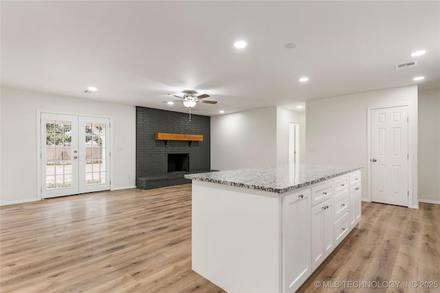 kitchen with light stone counters, a kitchen island, white cabinetry, open floor plan, and a brick fireplace