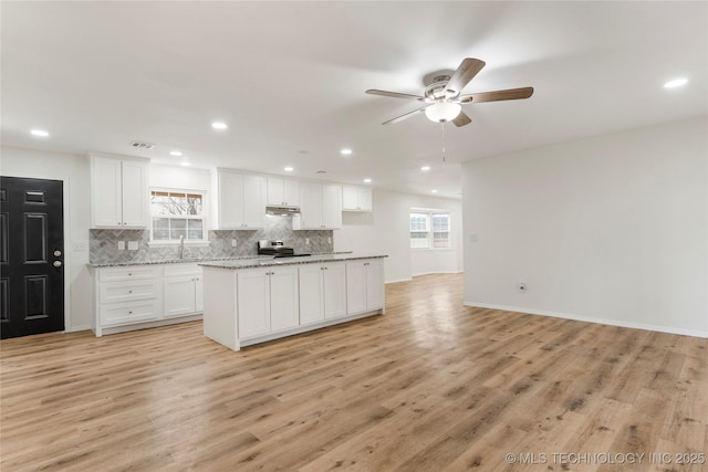 kitchen with light wood finished floors, tasteful backsplash, visible vents, light stone counters, and white cabinetry