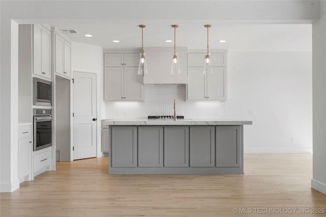 2038 E 129th St, Jenks, OK 74037 - kitchen with stainless steel appliances, light wood-style floors, an island with sink, decorative light fixtures, and recessed lighting