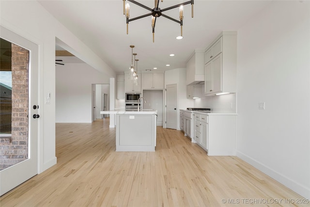 2038 E 129th St, Jenks, OK 74037 - kitchen with stainless steel appliances, a chandelier, light wood-style floors, light countertops, and a center island with sink