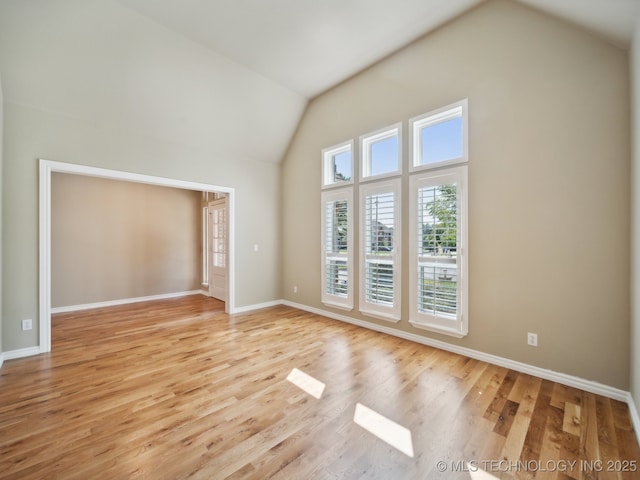 empty room with high vaulted ceiling, light wood-type flooring, and baseboards