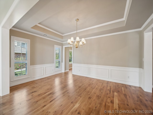 unfurnished room with visible vents, a healthy amount of sunlight, a tray ceiling, and wood finished floors