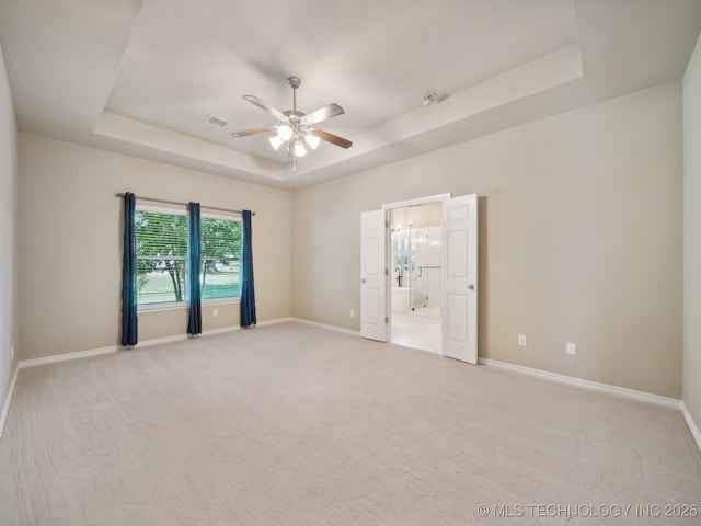 spare room with visible vents, a ceiling fan, a tray ceiling, baseboards, and light colored carpet