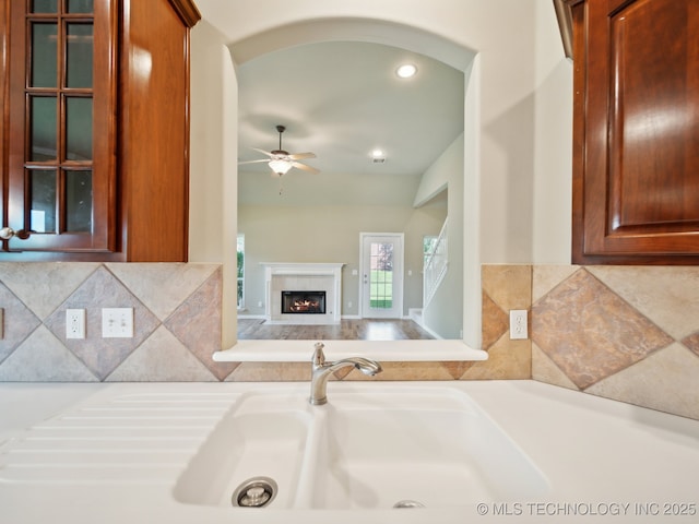 kitchen with a warm lit fireplace, arched walkways, backsplash, light countertops, and a sink