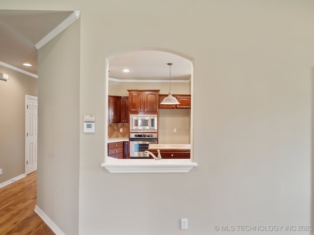 kitchen with stainless steel appliances, light countertops, ornamental molding, decorative backsplash, and decorative light fixtures