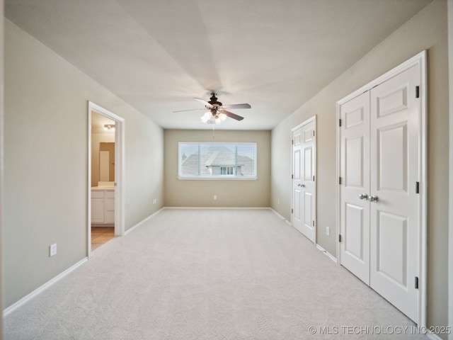 unfurnished bedroom featuring carpet, baseboards, ensuite bath, ceiling fan, and two closets