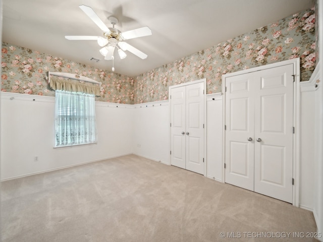 empty room with light carpet, wallpapered walls, visible vents, and wainscoting