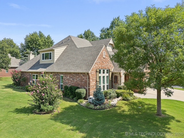 view of front of property with brick siding, a front lawn, and roof with shingles