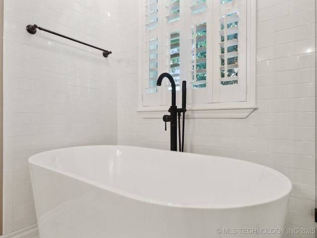 full bathroom featuring a freestanding tub, tile walls, and a sink