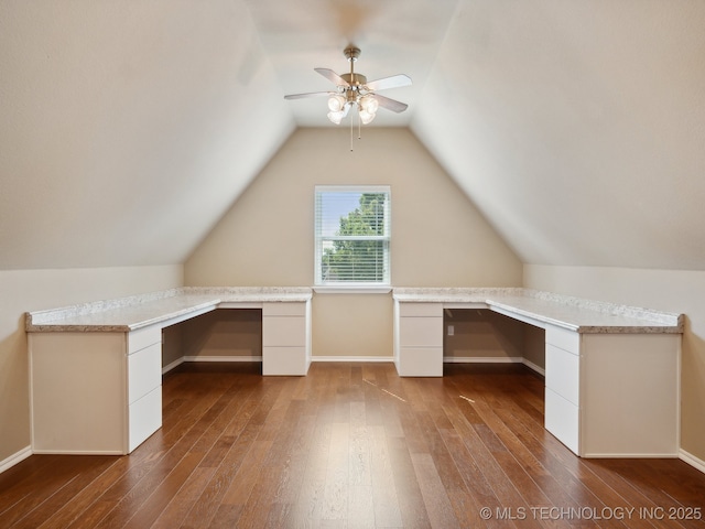 unfurnished office featuring dark wood-type flooring, built in desk, lofted ceiling, and ceiling fan