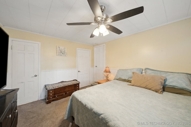 bedroom featuring ornamental molding, a wainscoted wall, light carpet, and a ceiling fan