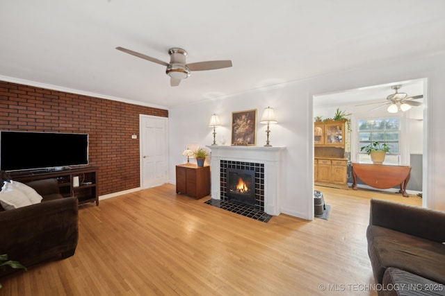 living room featuring light wood finished floors, a tile fireplace, a ceiling fan, and crown molding