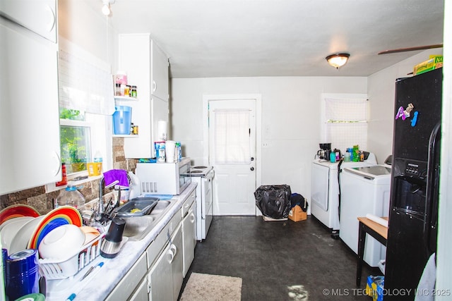 kitchen featuring a sink, black fridge, washing machine and clothes dryer, and white cabinetry