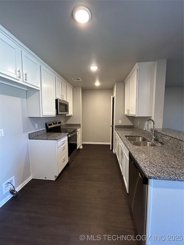 kitchen with dark wood-type flooring, a sink, white cabinetry, stainless steel appliances, and dark stone counters