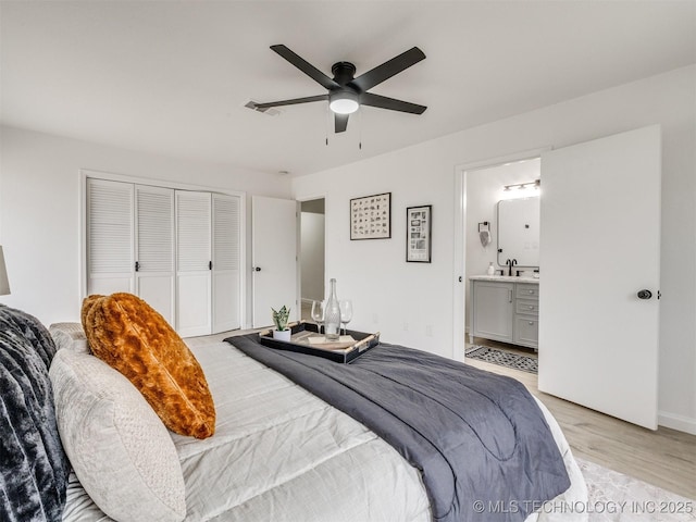 bedroom with a closet, visible vents, light wood-style flooring, a sink, and ensuite bath