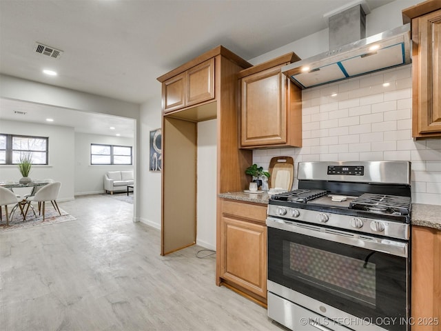 kitchen with light wood finished floors, tasteful backsplash, visible vents, wall chimney exhaust hood, and gas stove