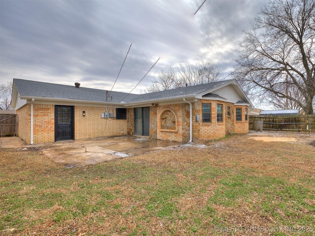 rear view of house featuring a yard, a patio, brick siding, and fence