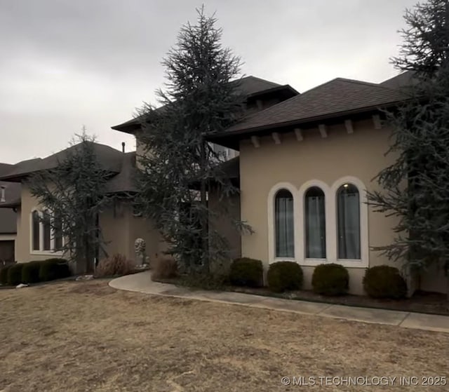 view of property exterior featuring a shingled roof, a lawn, and stucco siding