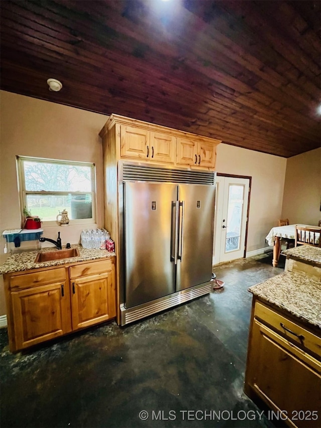 kitchen featuring light stone counters, wood ceiling, a sink, stainless steel built in refrigerator, and concrete floors