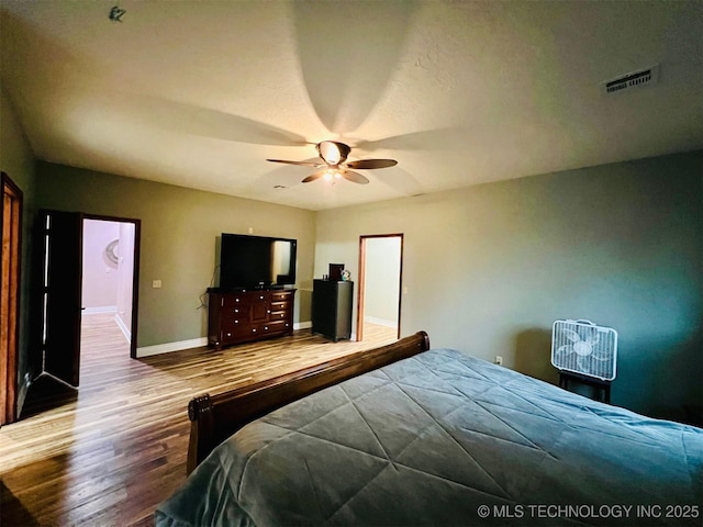 bedroom with ceiling fan, wood finished floors, visible vents, and baseboards