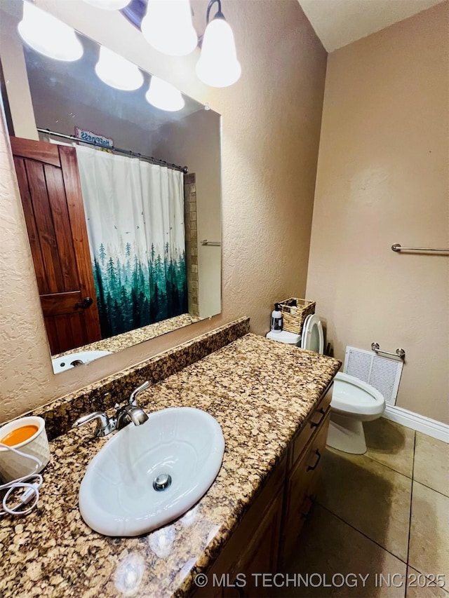 bathroom with a textured wall, toilet, vanity, tile patterned flooring, and baseboards