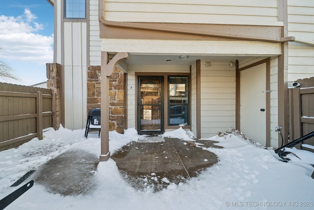 snow covered property entrance featuring stone siding and fence