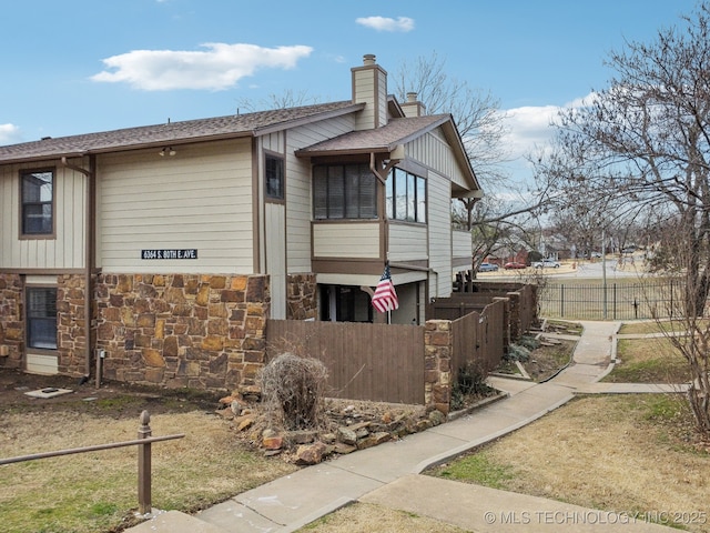 view of home's exterior with stone siding, a fenced front yard, a chimney, and roof with shingles