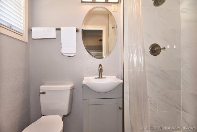 full bathroom with a tile shower, vanity, and toilet