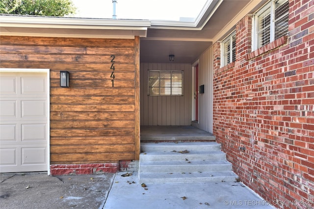 entrance to property featuring a garage and brick siding