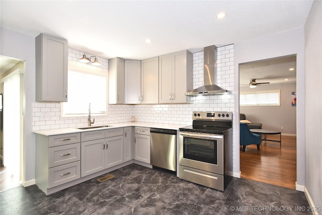 kitchen featuring wall chimney exhaust hood, stainless steel appliances, light countertops, gray cabinetry, and a sink