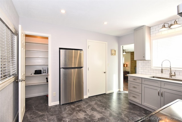 kitchen featuring gray cabinetry, a sink, light countertops, freestanding refrigerator, and decorative backsplash