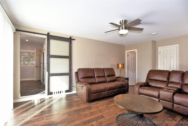 living room with ceiling fan, a barn door, dark wood finished floors, and baseboards