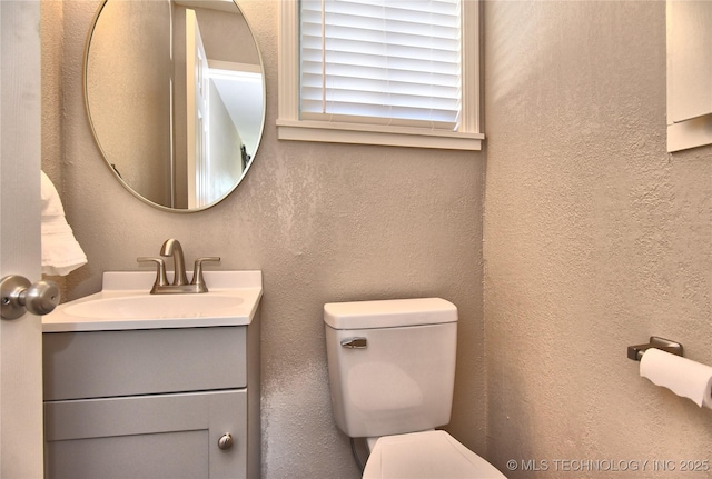 half bathroom with a textured wall, vanity, and toilet