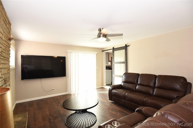 living room featuring a barn door, dark wood-style flooring, a ceiling fan, and baseboards