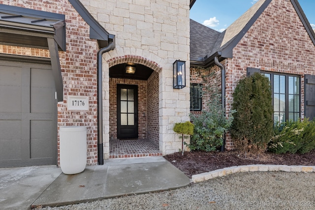 doorway to property with a garage, stone siding, a shingled roof, and brick siding