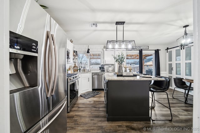 kitchen with visible vents, a center island, decorative light fixtures, stainless steel appliances, and white cabinetry