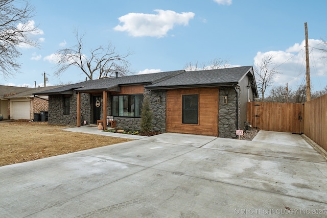 view of front facade featuring roof with shingles, concrete driveway, a front yard, fence, and stone siding