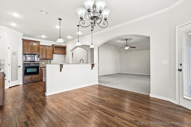 kitchen featuring arched walkways, stainless steel microwave, open floor plan, oven, and hanging light fixtures