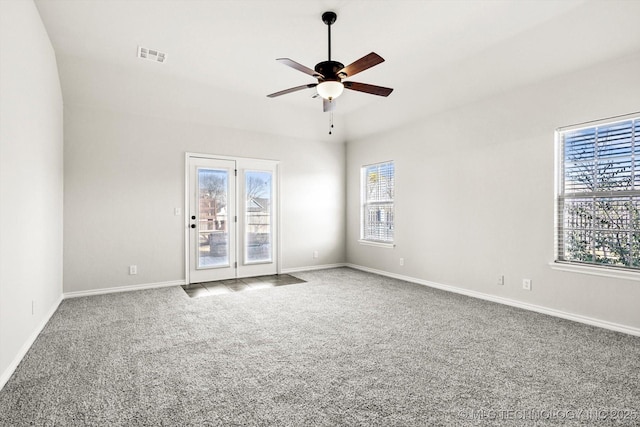 carpeted spare room featuring ceiling fan, plenty of natural light, visible vents, and baseboards